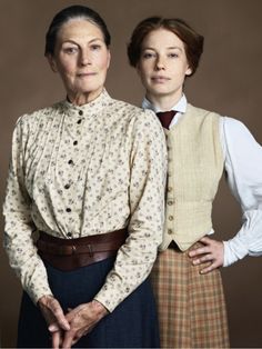 two women standing next to each other in front of a brown background