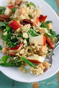 a white plate topped with quinoa, apples and spinach salad covered in nuts