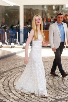 a woman in a white dress is walking with a man