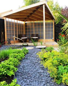 a garden with rocks and plants in the foreground, next to a covered patio