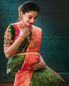 a woman in a green and red sari sitting on the ground with her hands clasped to her chest