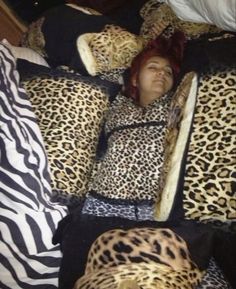 a woman laying in bed with leopard print pillows and blankets on top of her head