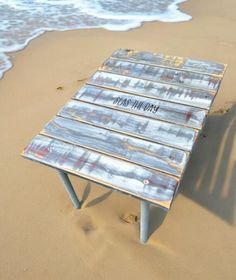 an old wooden bench sitting on top of a sandy beach next to the ocean with waves coming in