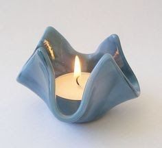 a blue candle holder with a single lit candle in it's center on a white surface