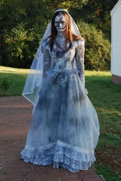 a woman dressed up as a bride in a wedding dress and veil, standing on a brick walkway