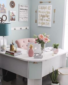 a white desk topped with lots of pink flowers next to a lamp and pictures on the wall