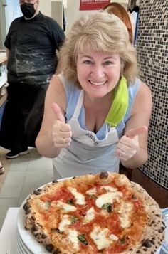 a woman sitting at a table with a pizza in front of her giving the thumbs up sign