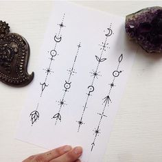 a hand holding a piece of paper with designs on it next to a purple rock