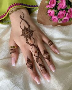 a woman's hand with henna on it and pink flowers in the background