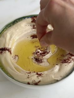 a person dipping something into a bowl filled with cream and brown sprinkles