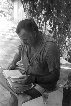 a man sitting at a table with a book in his hand and an empty bottle next to him