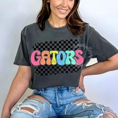 a woman sitting on top of a chair wearing ripped jeans and a t - shirt with the word gators painted on it