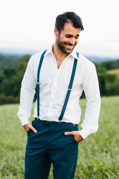 a man standing in a field with his hands on his hips wearing suspenders and a white shirt