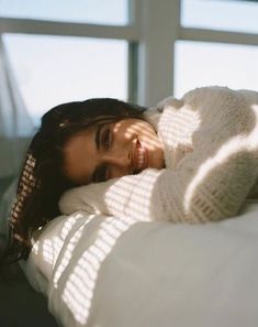 a woman laying on top of a bed next to a window with sunlight streaming through it