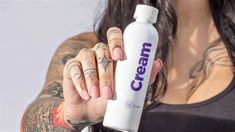 a woman with tattoos holding up a cream bottle