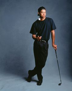 a man in black is holding a golf club and posing for the camera with his hat on