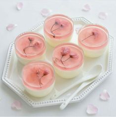 four candles with pink flowers on them sitting on a white plate next to spoons