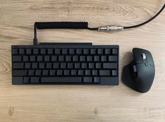 a computer keyboard and mouse on a wooden surface with wires attached to the back side