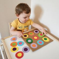 a young child is playing with colorful circles on a cardboard board in front of a white wall