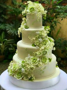 a three tiered wedding cake with green flowers on the top and bottom, sitting on a table