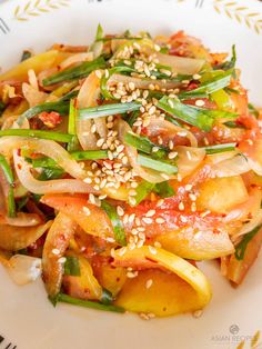 a white plate topped with pasta and veggies covered in sesame seed toppings