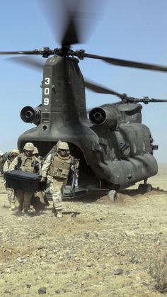 two soldiers are carrying a large object from a helicopter in the middle of the desert