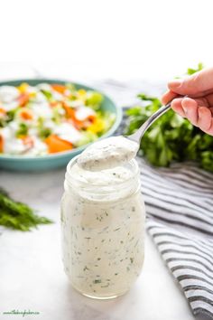 homemade ranch dressing in a glass jar with a spoon and salad on the table behind it