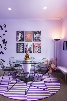 a dining room with purple walls and pictures on the wall, including a round glass table surrounded by metal chairs