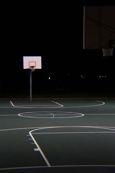 an empty basketball court at night with the lights on and hoop in the air above it