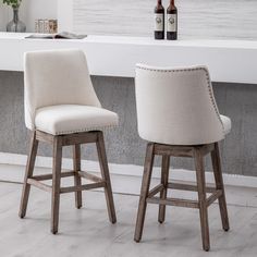 two white bar stools in front of a counter with bottles on it and a window behind them