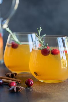 two glasses filled with drinks sitting on top of a wooden table next to cinnamon sticks and cranberries