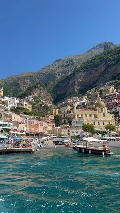 boats are parked on the water in front of some buildings and mountains, with blue skies above them