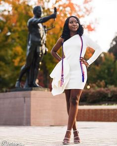 a woman standing in front of a statue with her hands on her hips wearing a white dress