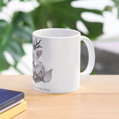 a white coffee mug sitting on top of a wooden table next to a blue book