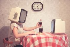 a woman sitting at a table with two televisions on top of her head and a soda bottle in front of her