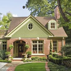 a brick house with green trim and white shutters on the front door is surrounded by greenery