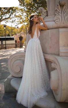 a woman standing next to a stone pillar wearing a white dress with an open back