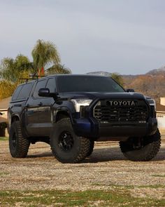 a large black truck parked on top of a dirt field