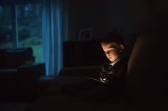 a young boy sitting on a couch in the dark looking at a tablet computer screen