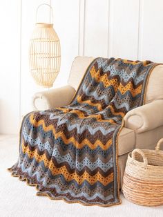 a couch with a crocheted blanket on it next to a basket and lamp