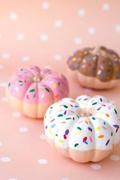 three donuts decorated with sprinkles on a pink surface