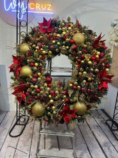 a christmas wreath with red and gold ornaments on a wooden floor in front of a neon sign