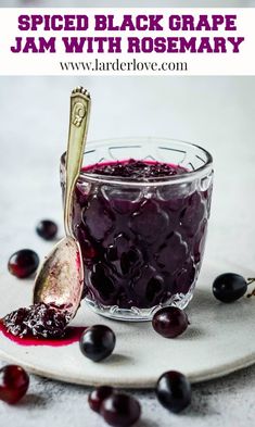 a glass jar filled with jam next to a spoon and cherries on a plate