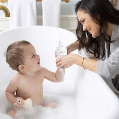 a woman is bathing a baby in the bathtub with a bottle of lotion