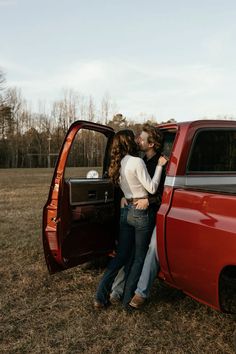 two people are kissing in the back of a red pickup truck with its doors open