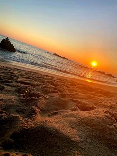 the sun is setting at the beach with sand and rocks in the foreground,