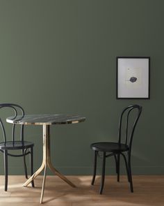 two black chairs and a round table in a room with green paint on the walls