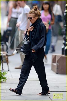 a woman walking down the street carrying a handbag and wearing black shoes with her hair in a bun