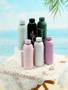 six different colored water bottles sitting on top of a white table next to the ocean