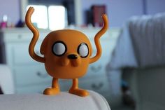 an orange toy with large eyes and big ears on it's head is standing in front of a bed